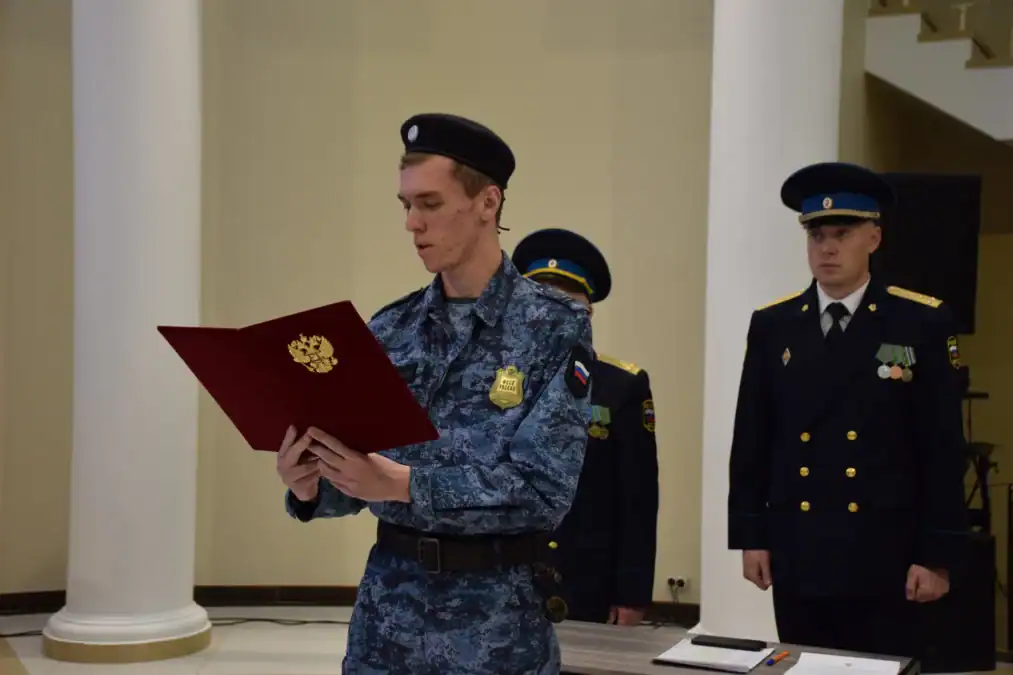 Сотрудник в камуфляжной форме читает текст из красной папки перед офицерами.
