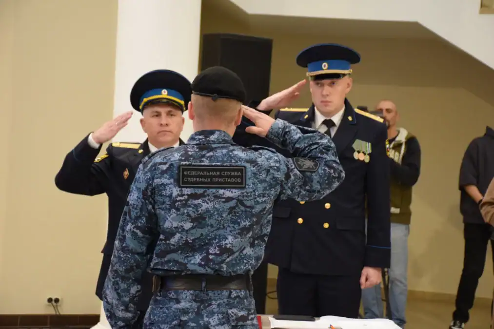 Сотрудник и два офицера в парадной форме отдают воинское приветствие.