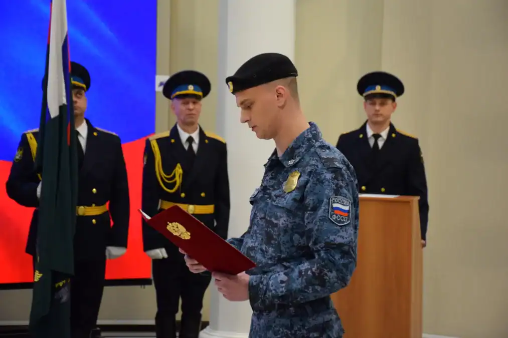Сотрудник в форме с эмблемой службы читает текст из красной папки.