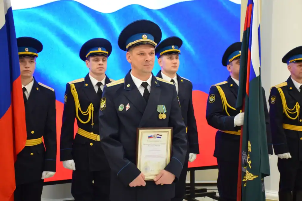 Офицер в парадной форме держит грамоту перед почётным караулом.
