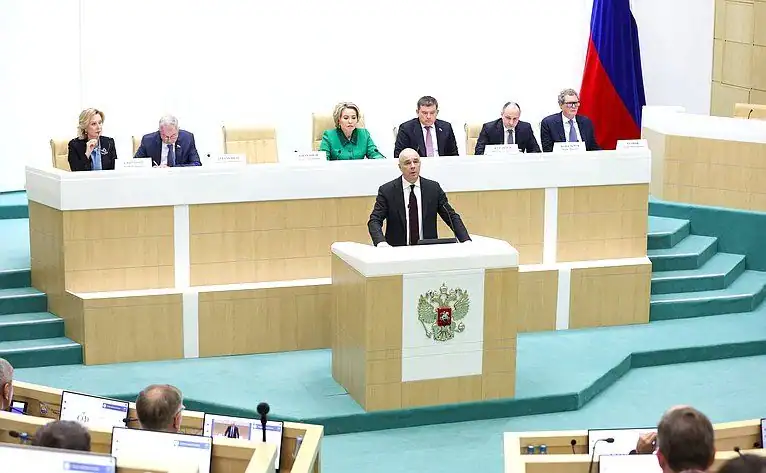 Мужчина выступает с трибуны перед сидящими за президиумом участниками заседания.