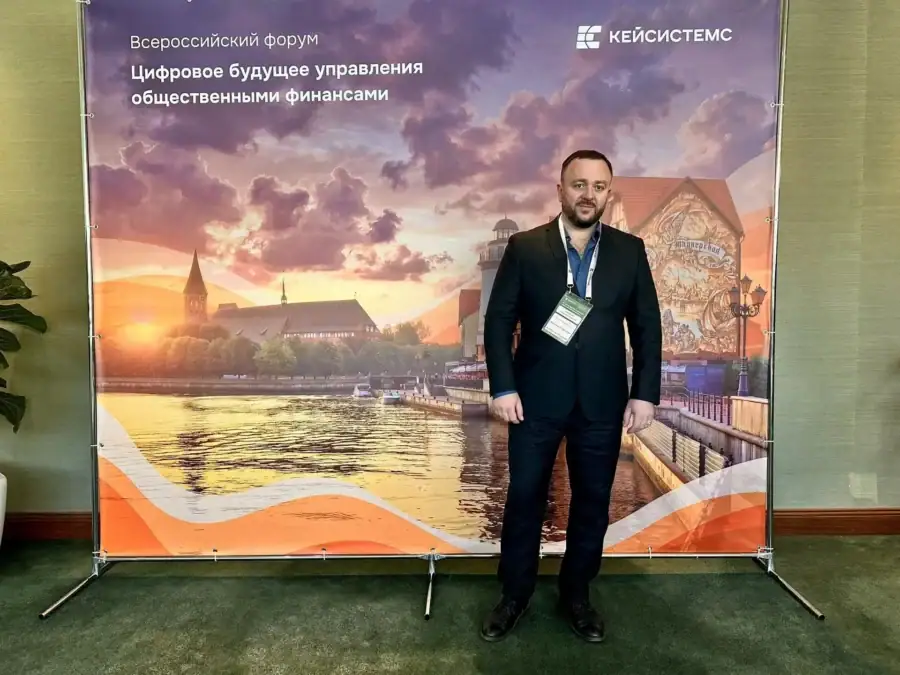 Мужчина с бейджем стоит у брендированного стенда Всероссийского форума.