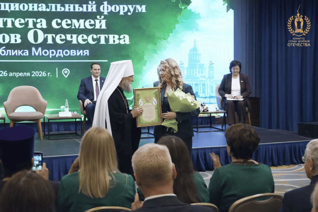 Женщине на сцене вручают рамочный сертификат и букет цветов.