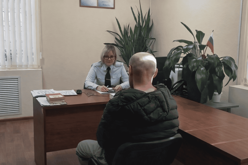Сотрудница в форме беседует с мужчиной за столом в кабинете.