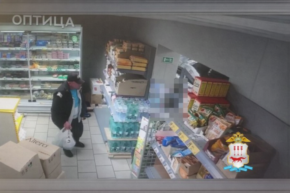 Мужчина с белым пакетом стоит между стеллажами в продуктовом магазине.