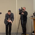 Операторы с камерами снимают мероприятие в конференц-зале.