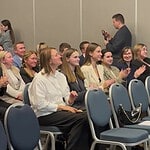 Участники форума сидят рядами и аплодируют в конференц-зале.