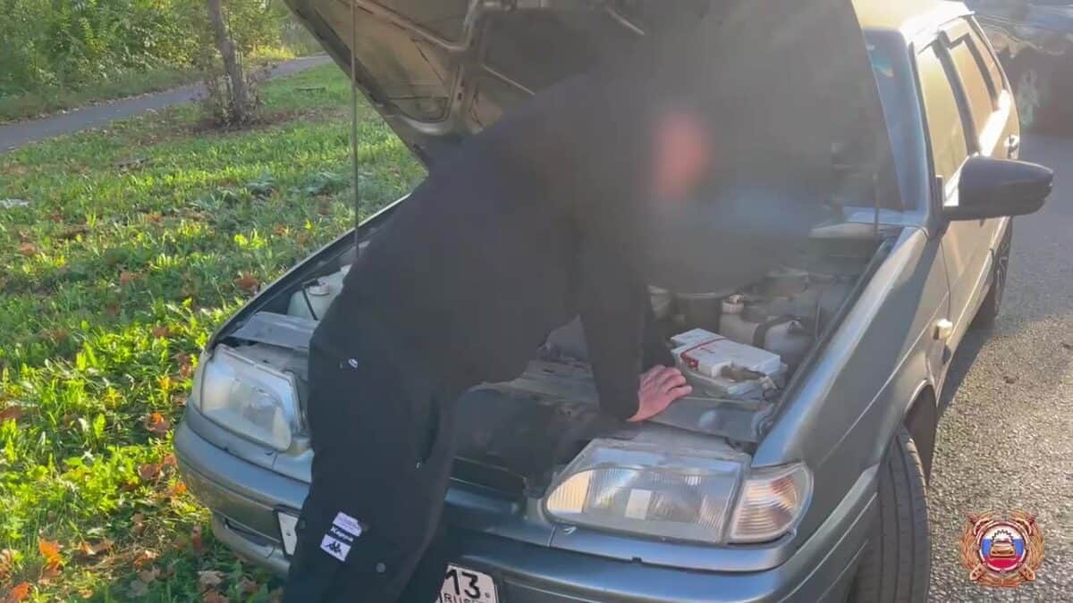 Человек осматривает двигатель автомобиля с поднятым капотом.