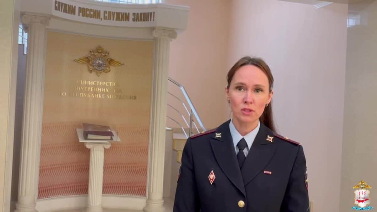 Сотрудница полиции в форме стоит в холле у стенда МВД.