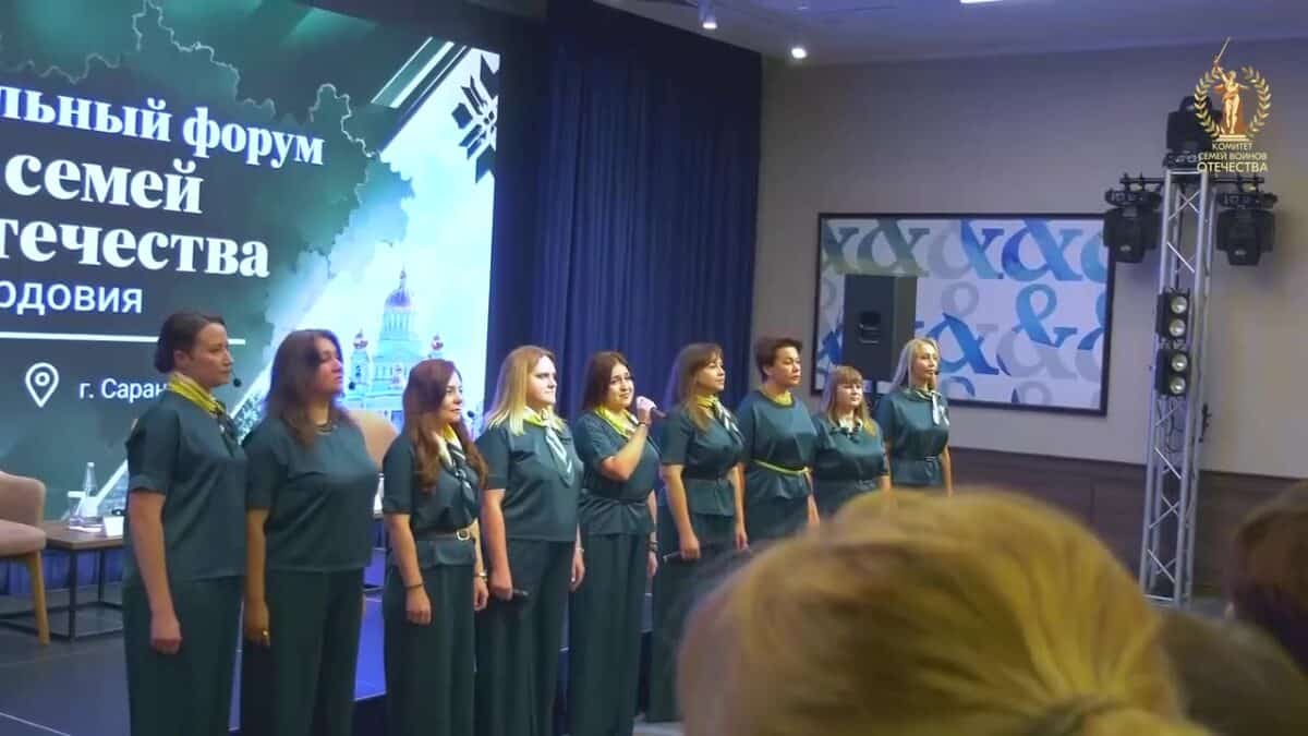 Группа женщин в одинаковых зелёных платьях выступает на сцене форума.