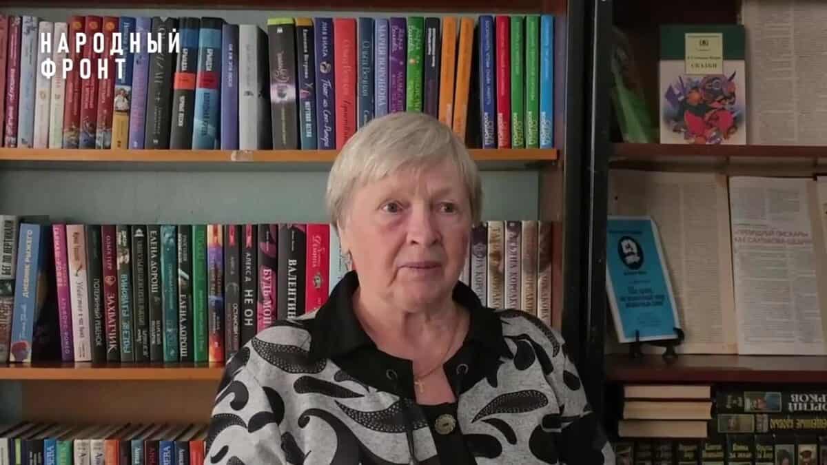 Пожилая женщина сидит перед книжными стеллажами в библиотеке.