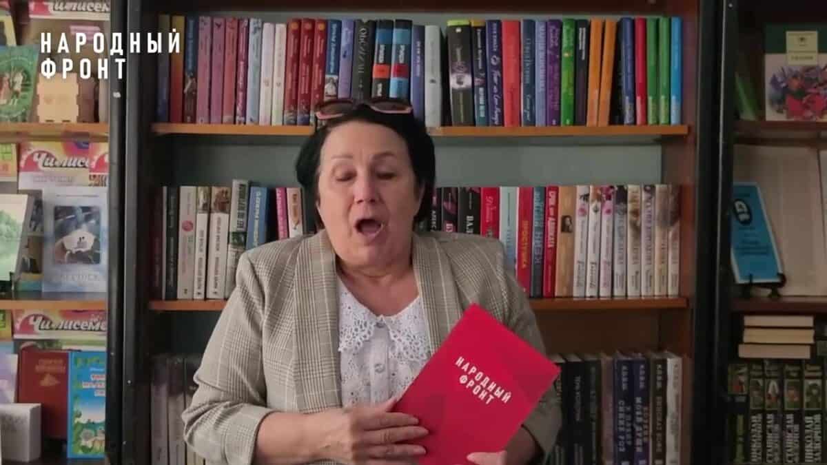 Женщина держит красную папку «Народный фронт» перед книжными полками.