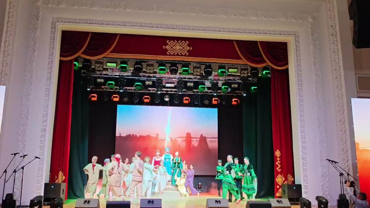 Участники концерта в народных костюмах стоят на освещенной сцене.