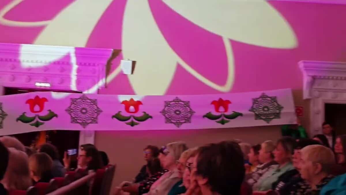 Зрители сидят в зале под длинным полотнищем с народным орнаментом.