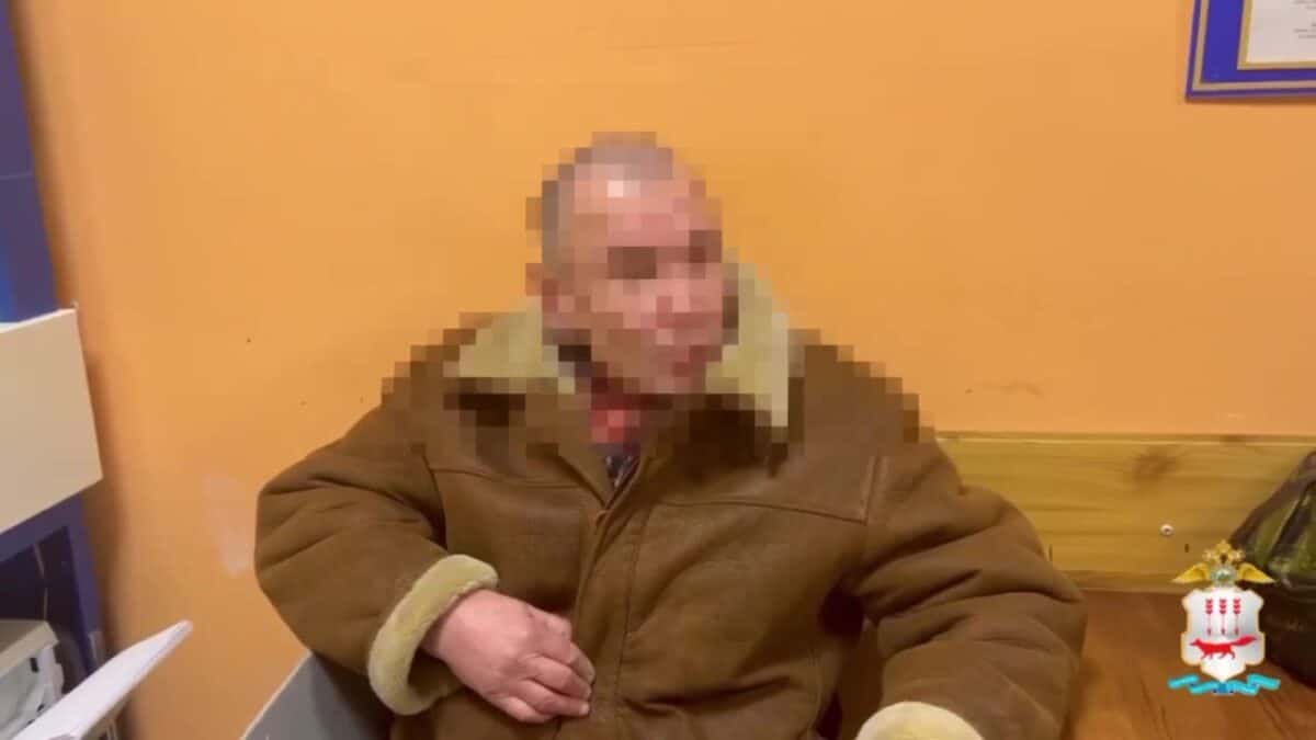 Мужчина в коричневой куртке сидит в помещении, его лицо скрыто пикселизацией.
