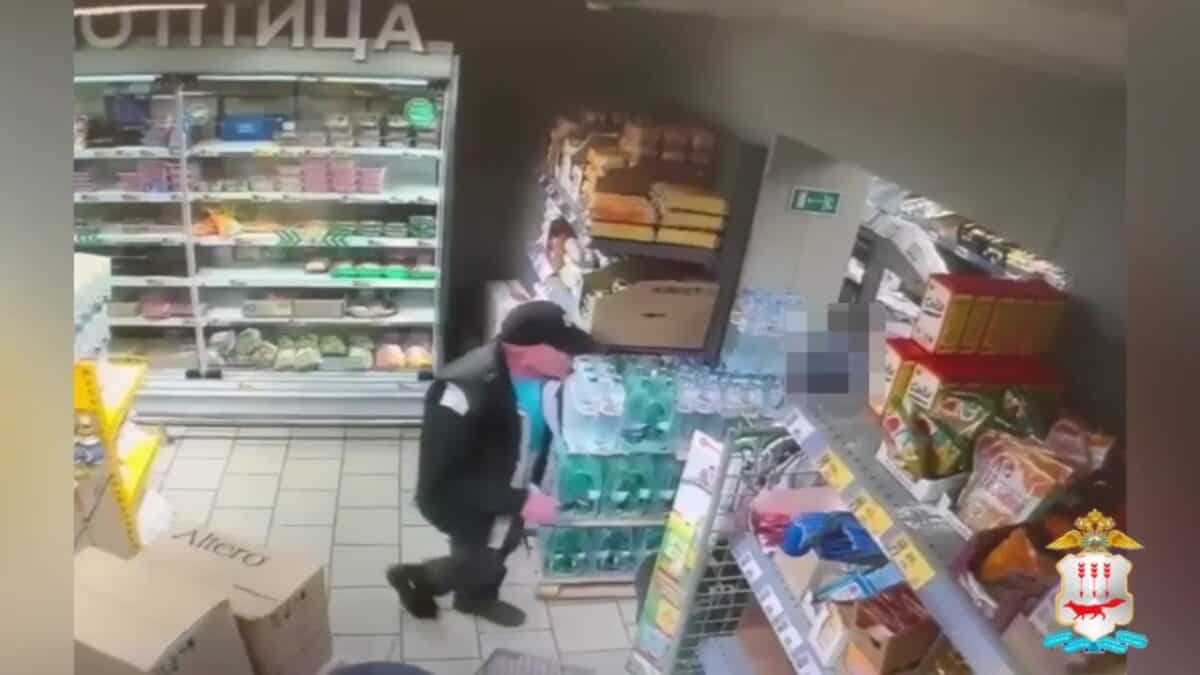 Мужчина в тёмной одежде стоит у стеллажей магазина рядом с холодильной витриной.