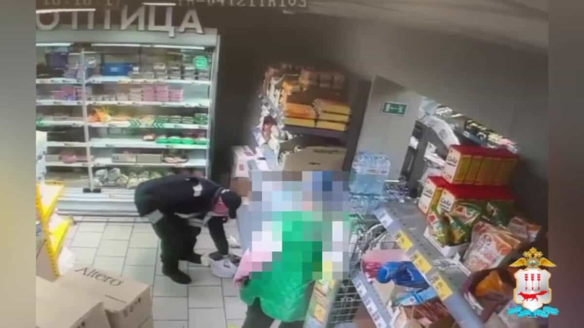 Мужчина наклоняется у стеллажа рядом с человеком, лицо которого скрыто пикселизацией.