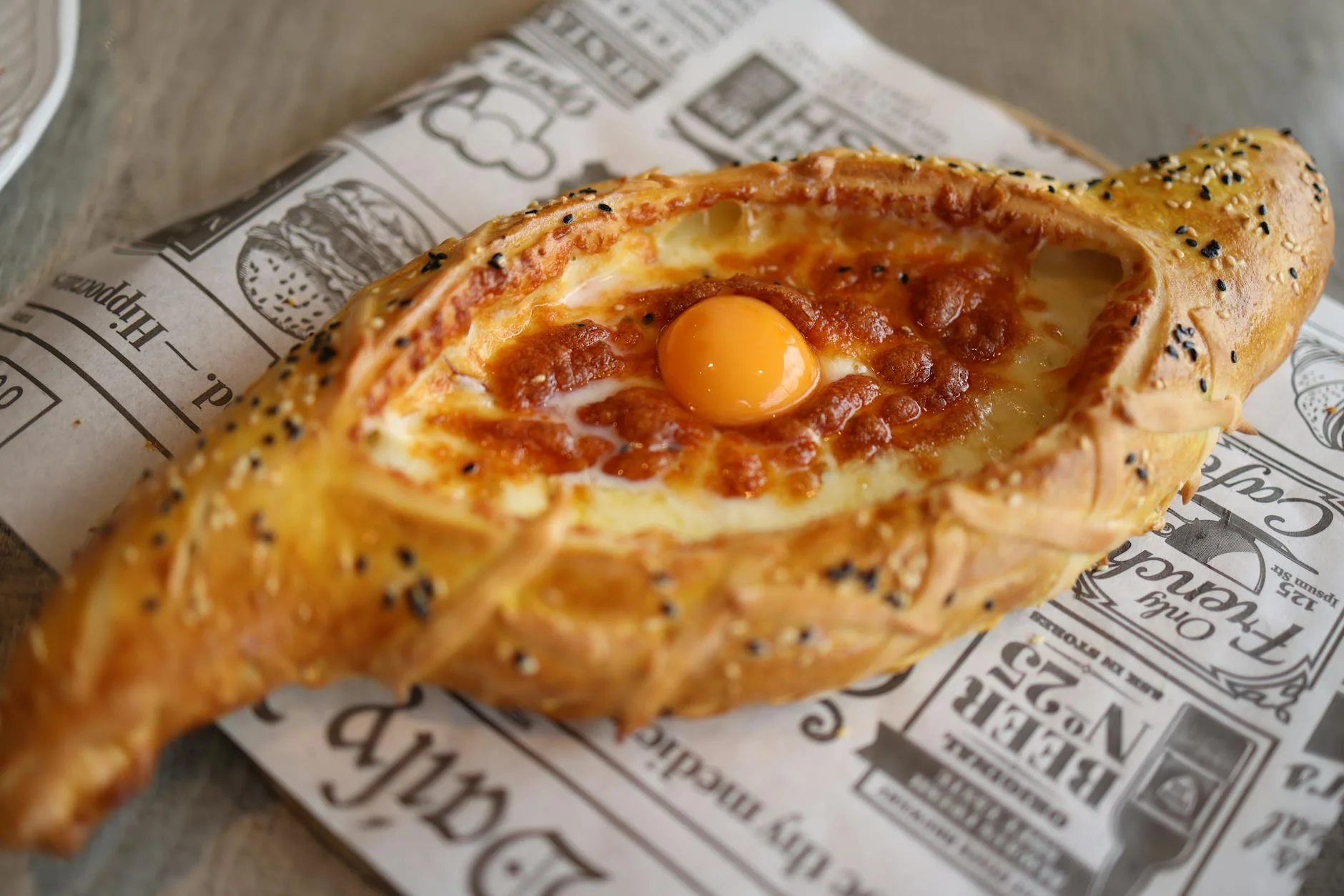 Delicious Georgian khachapuri topped with a golden egg yolk and melted cheese on a patterned paper.