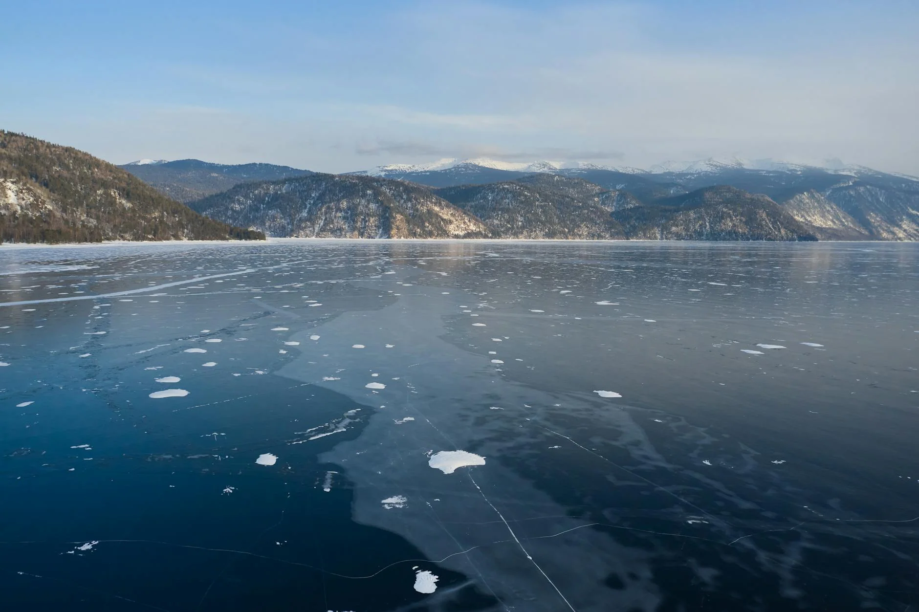 Amazing view of mountain ridge located on coast of frozen lake against blue sky in winter day