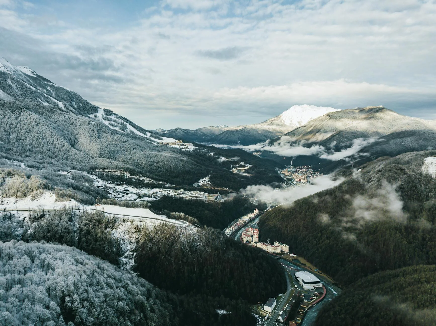 Breathtaking aerial view of a snowy mountain valley, showcasing cloud-wrapped peaks and a serene winter landscape.
