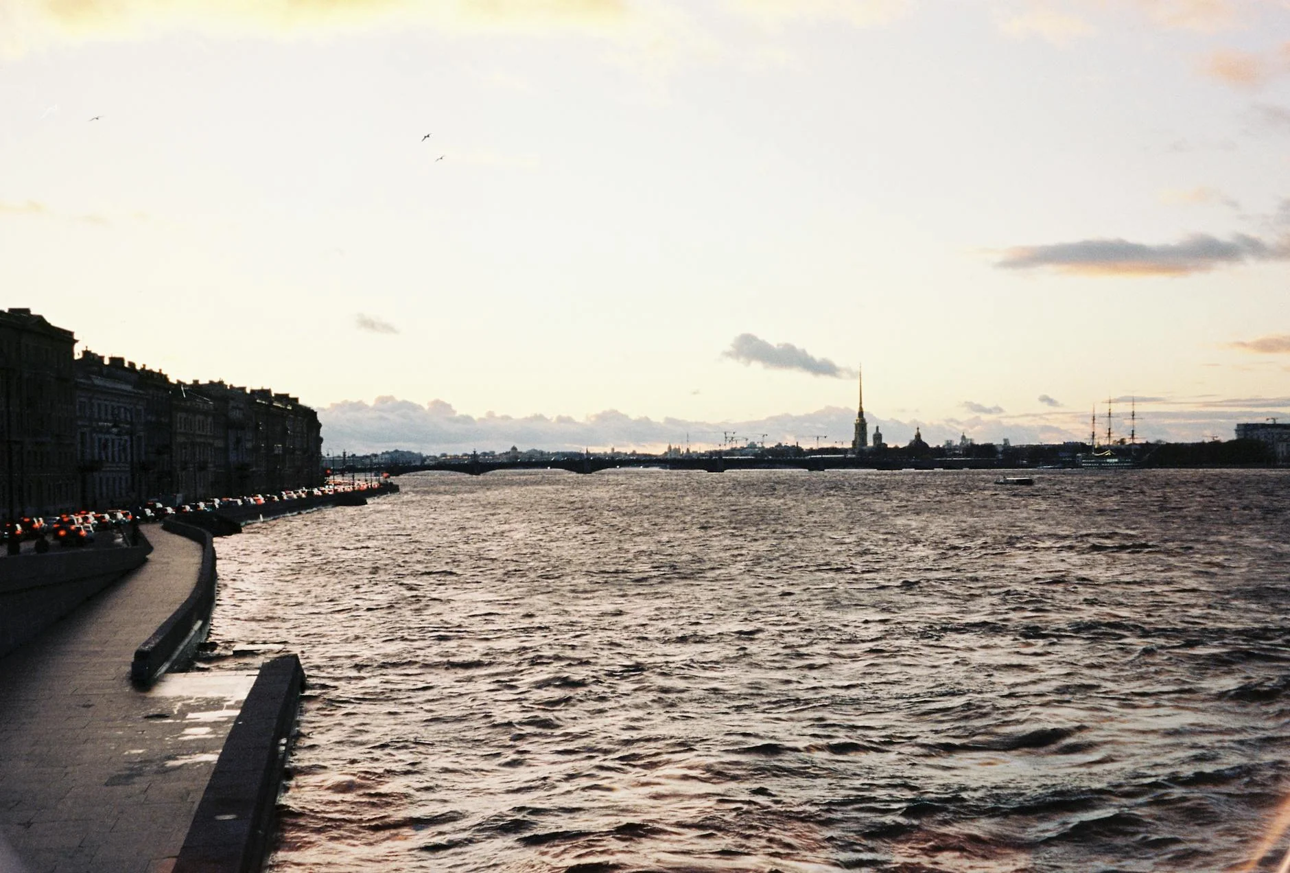 Serene riverside scene in St. Petersburg with distant city skyline and golden dusk sky.