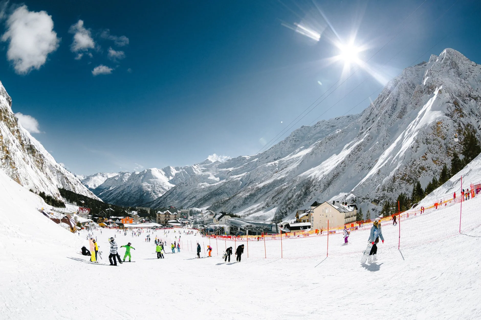 A sunny winter day at a bustling ski resort with snowcapped mountains and skiers enjoying the slopes.