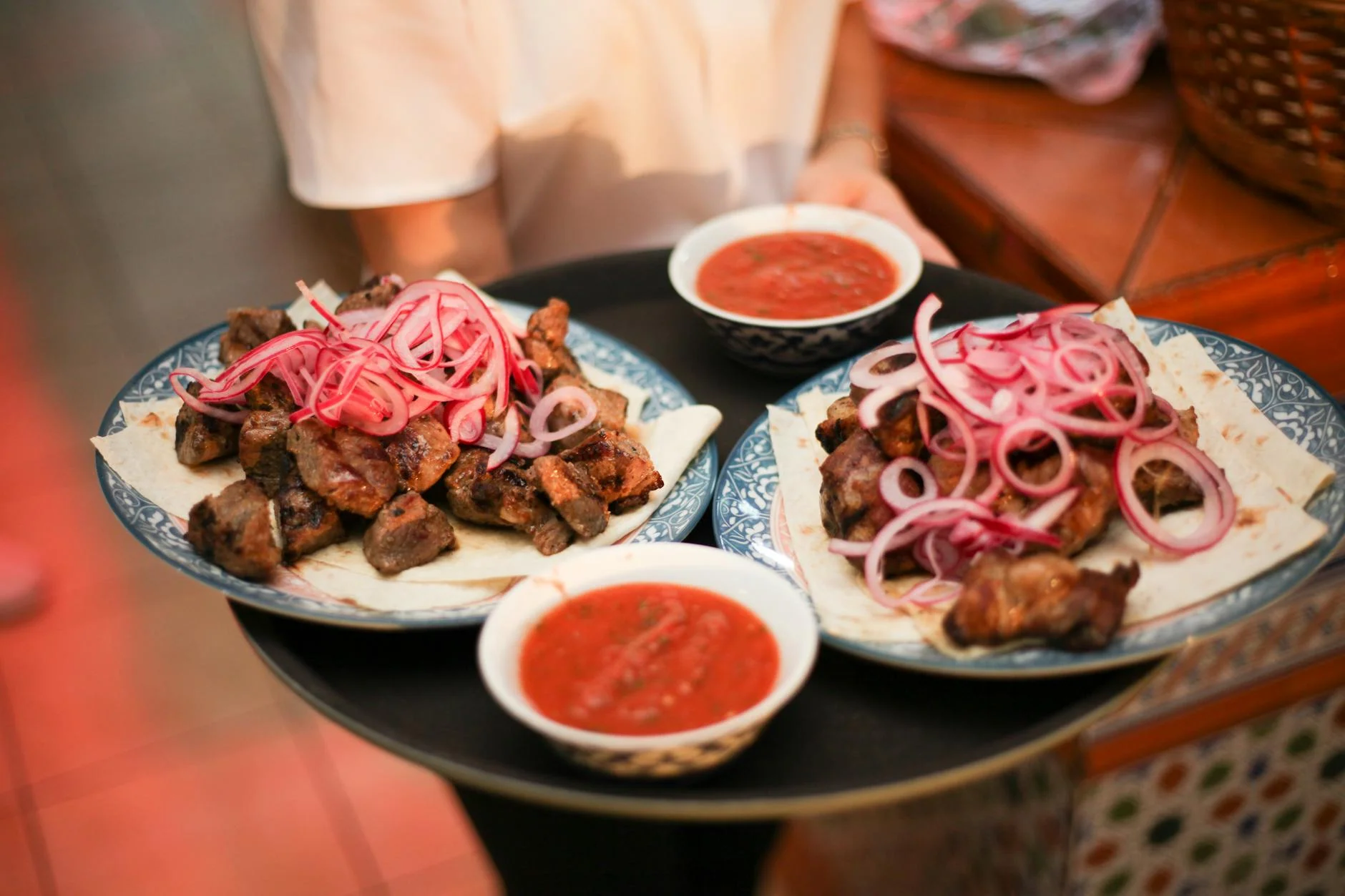 A mouthwatering presentation of grilled meat with onion garnish and sauce bowls.