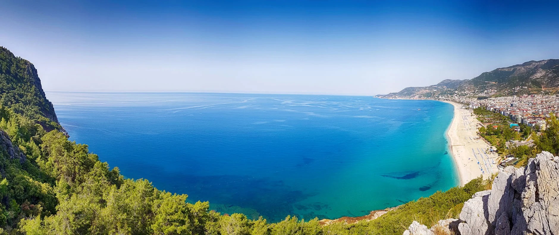 Stunning panoramic view of Alanya's turquoise coastline, beach, and distant cityscape in Antalya, Turkey.