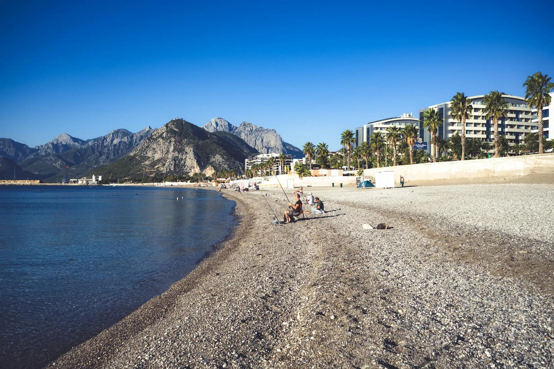A peaceful beach scene with people fishing and relaxing, set against distant mountains.