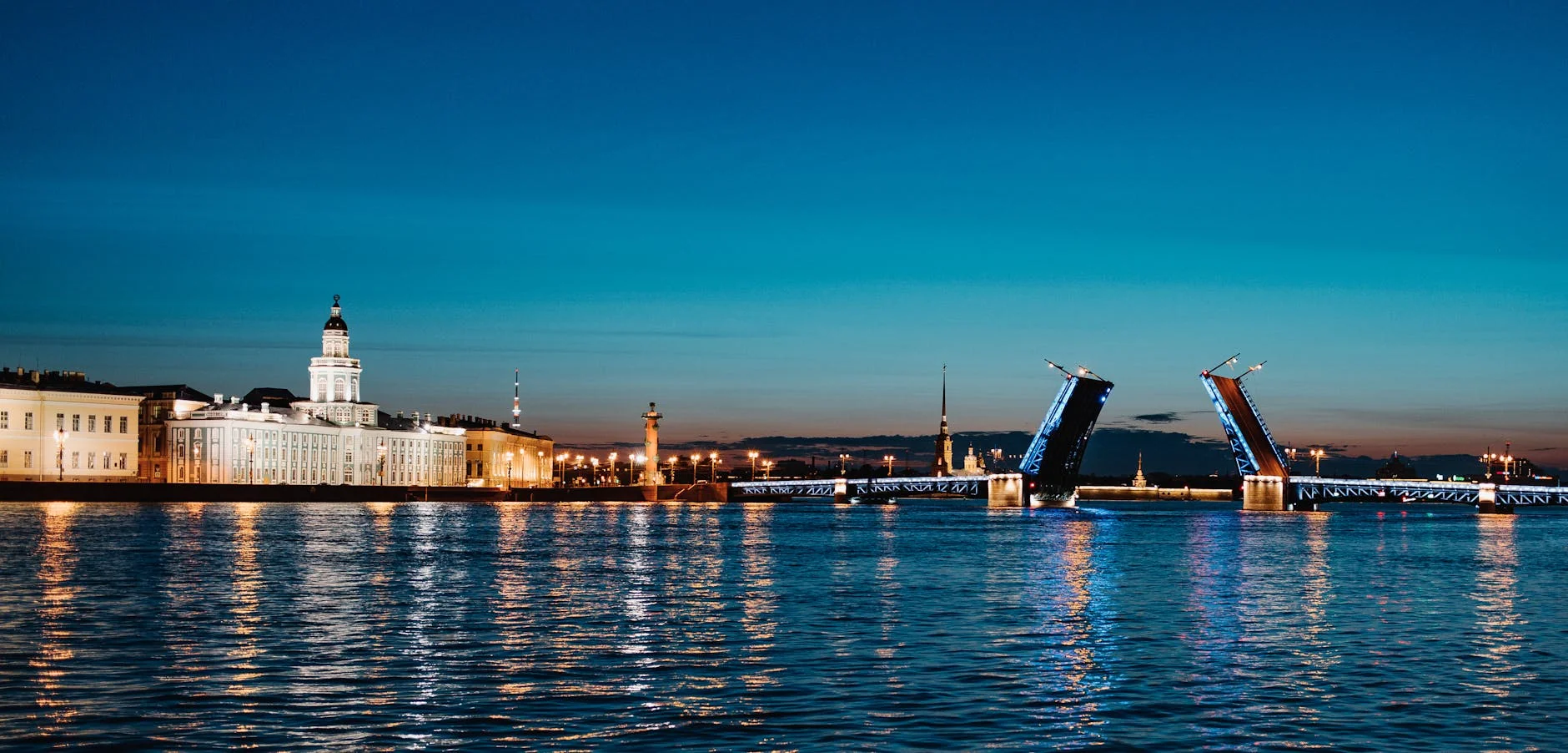 The Palace Bridge in Saint Petersburg opens at twilight, illuminating the skyline and reflecting on the Neva River.