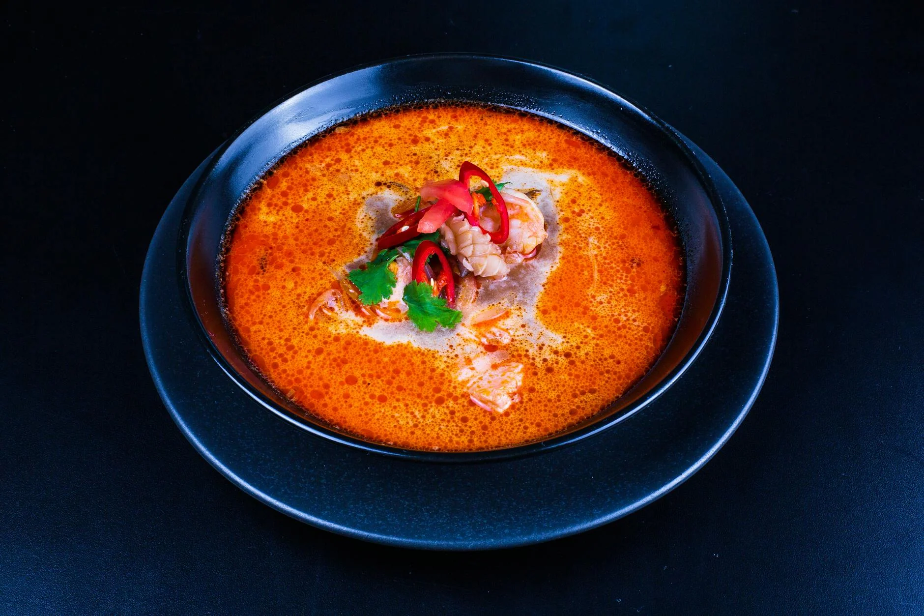 A vibrant and spicy seafood soup served in a black bowl on a dark background.